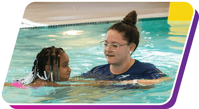 A YMCA staff member teaching a young girl how to swim